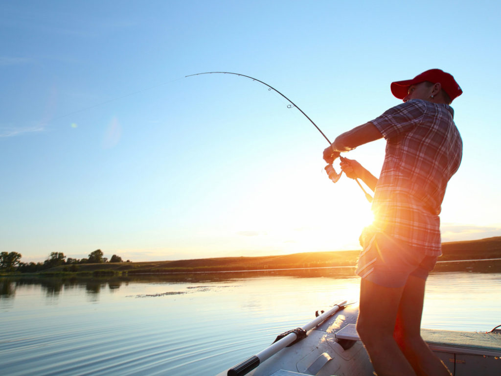 Young man fishing on a lake from the boat at sunset